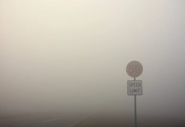 A speed limit sign barely visible through thick morning fog