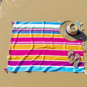Overhead shot of a colorful beach towel, flip-flops, and a straw hat placed on smooth sand by the shoreline