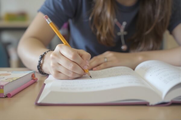 Close-up of a student writing notes in a book with a pencil in classroom