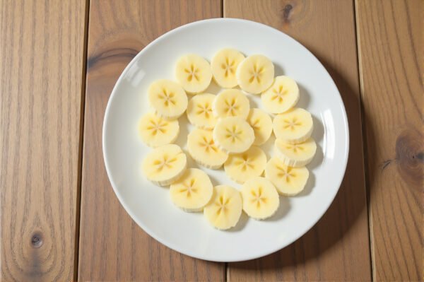 Banana slices arranged neatly on a white ceramic plate, top-down view