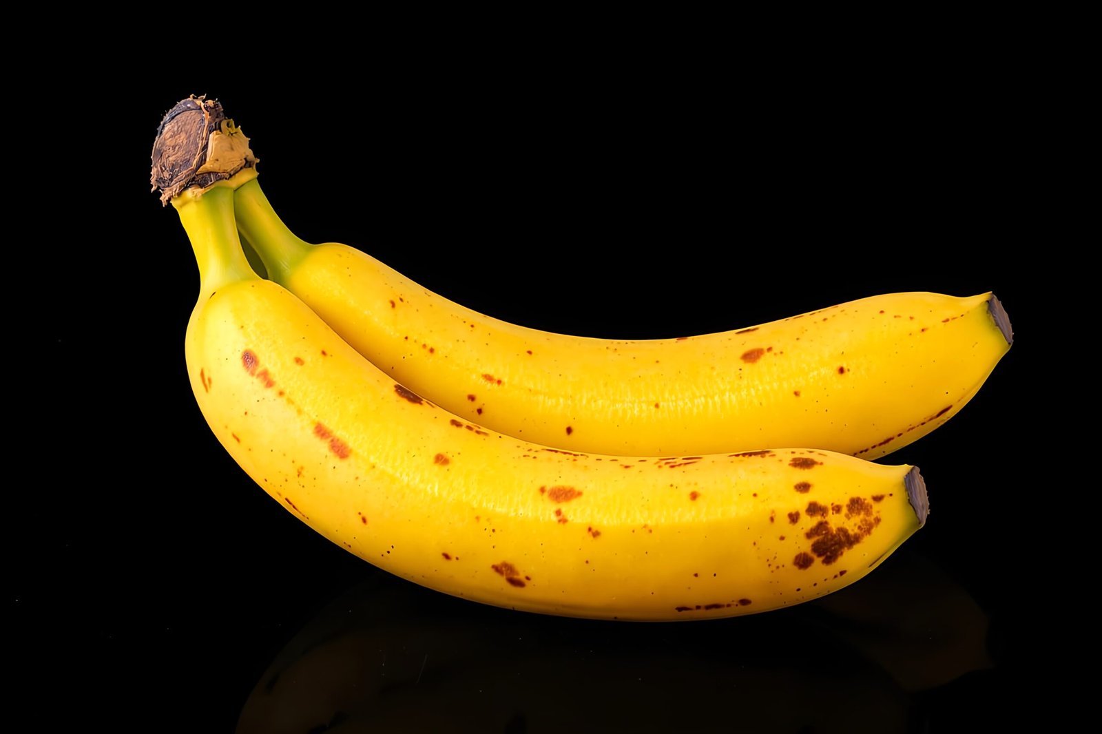 Two overripe bananas with brown spots isolated on black background