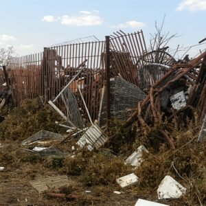 Photorealistic junkyard scene with broken rusted fences, crushed metal objects, and weeds growing through the pile