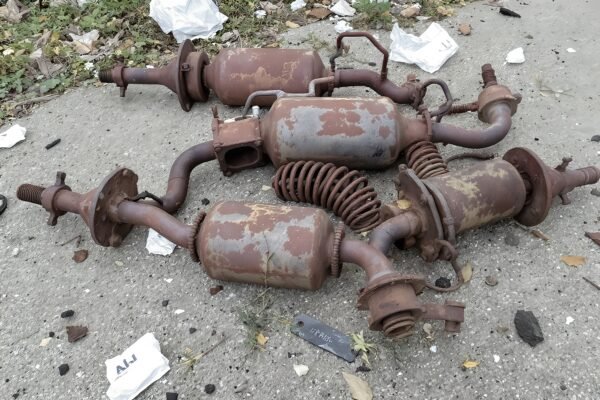 Rusted car parts including mufflers, springs, and axles dumped on concrete ground