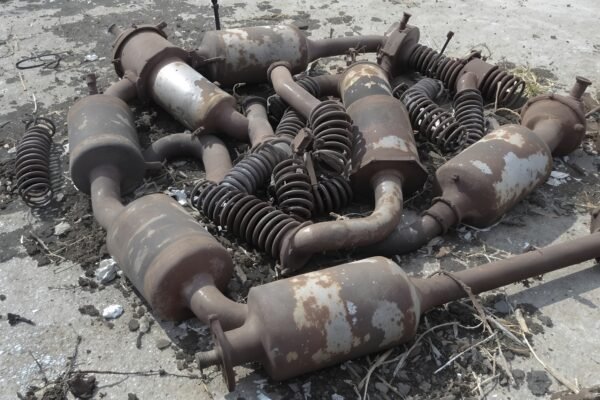 Rusted car parts including mufflers, springs, and axles dumped on concrete ground