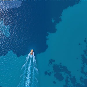 Aerial top down view of small boat floating in crystal clear turquoise ocean waters