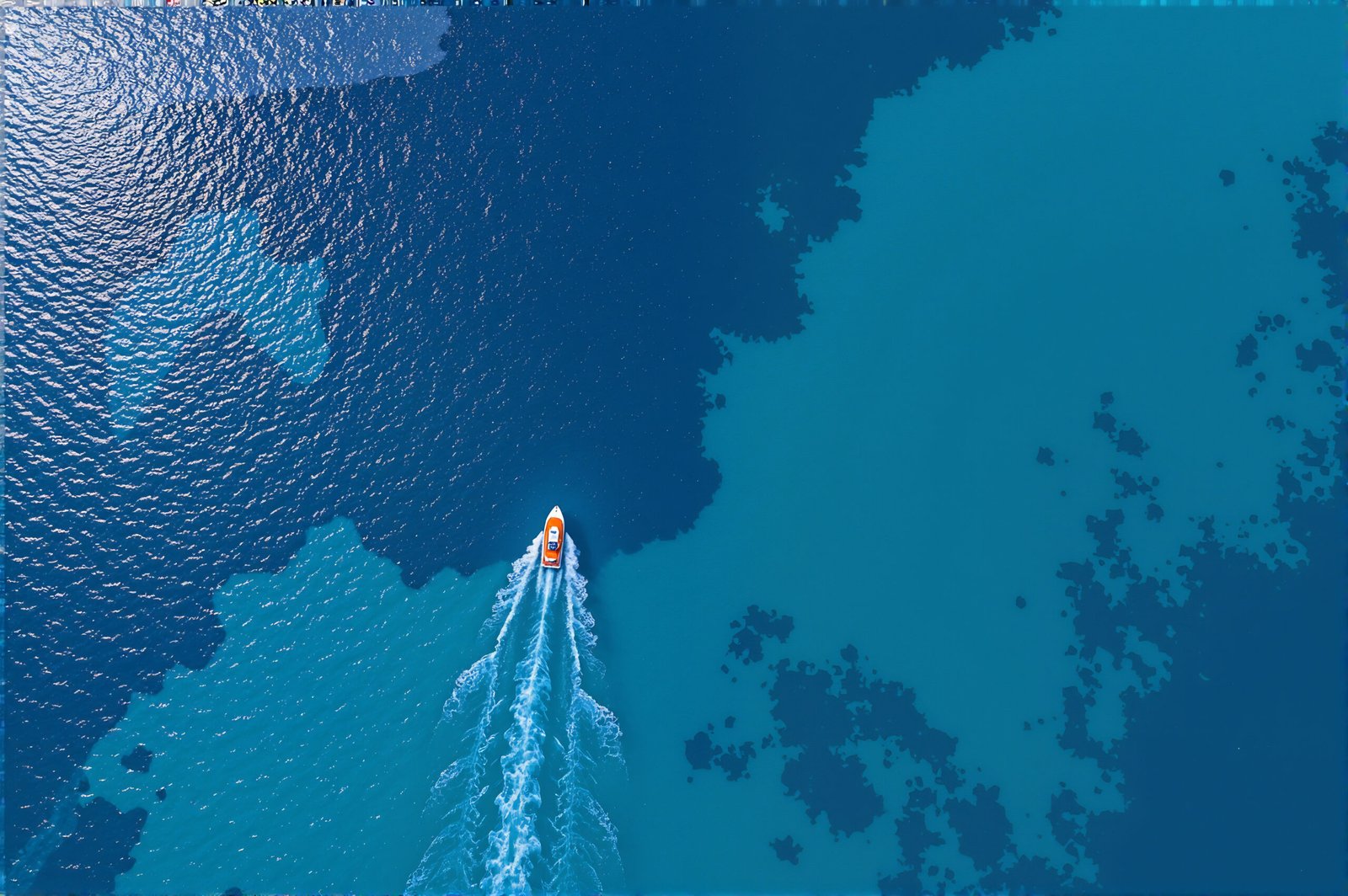 Aerial top down view of small boat floating in crystal clear turquoise ocean waters