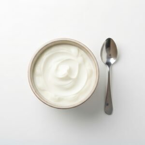 greek yogurt in a small ceramic bowl with spoon beside it top down shot bright soft daylight pure white background