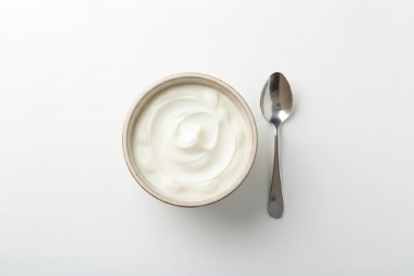greek yogurt in a small ceramic bowl with spoon beside it top down shot bright soft daylight pure white background
