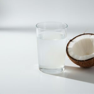 Transparent glass filled with coconut water placed beside a cracked coconut half white background soft natural shadows high resolution realism.