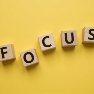 Alphabet wooden cubes spelling FOCUS loosely arranged with uneven spacing slightly rotated blocks bold black letters yellow background productivity concept