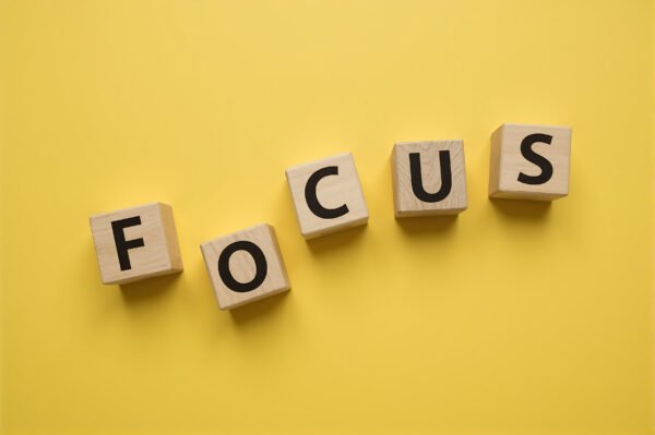 Alphabet wooden cubes spelling FOCUS loosely arranged with uneven spacing slightly rotated blocks bold black letters yellow background productivity concept